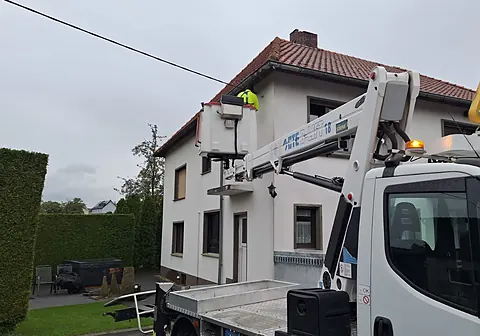 Arbeitskorb eines Hubsteigers am Hausanschluss einer Freileitung