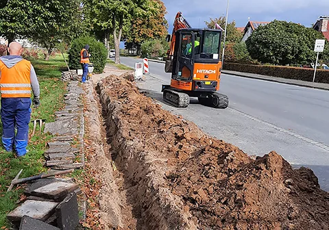 Kabelgraben entlang einer Straße mit Minibagger