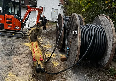 Kabeltrommeln am Graben, Kabel wird eingezogen, Minibagger im Hintergrund