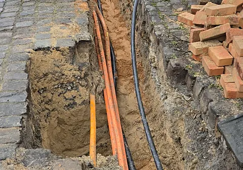 Orange Schutzrohre und Kabel im Graben neben dem Gehweg